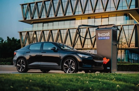 Zwarte elektrische wagen die opgeladen wordt aan een BoostCharge-snellader, geplaatst voor een modern kantoorgebouw, benadrukt de impact van de afschaffing EV-premie.